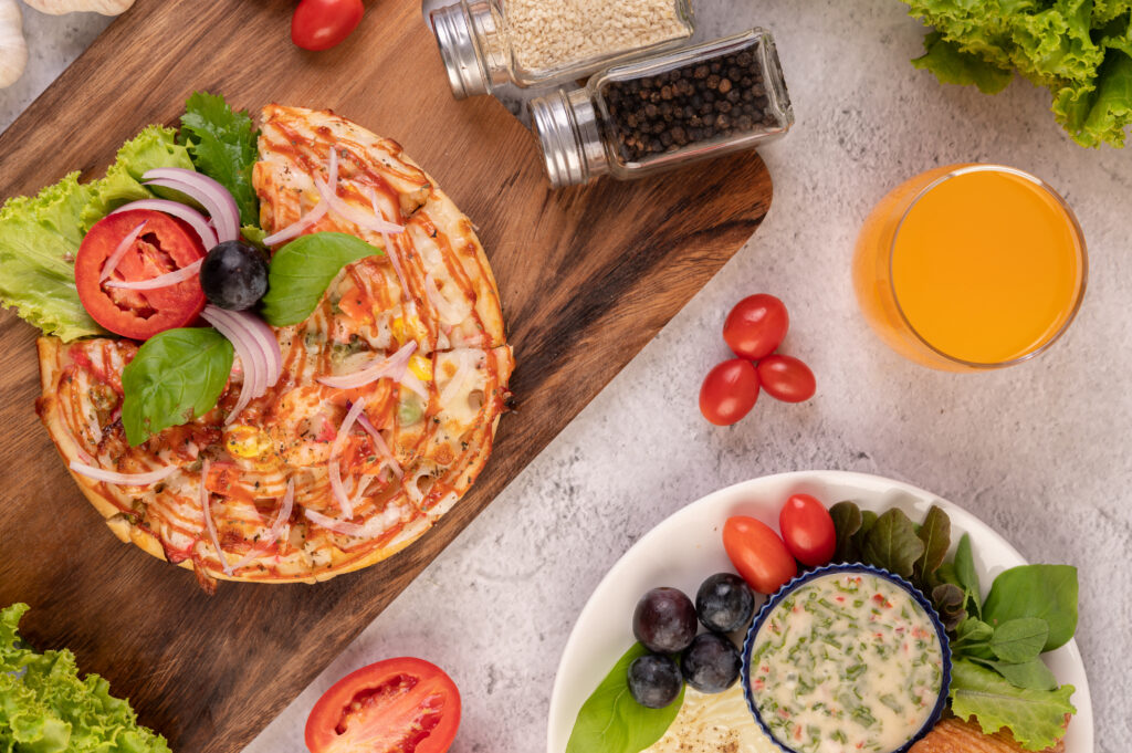 The pizza is in a wooden tray topped with red onions, black grapes, tomatoes, and lettuce.